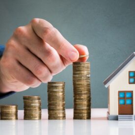 Stacks of coins next to a mini home, depicting increasing home values